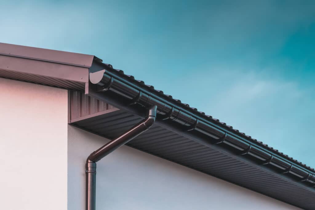 Chocolate colored plastic gutter on the roof of the building and downpipe on the wall